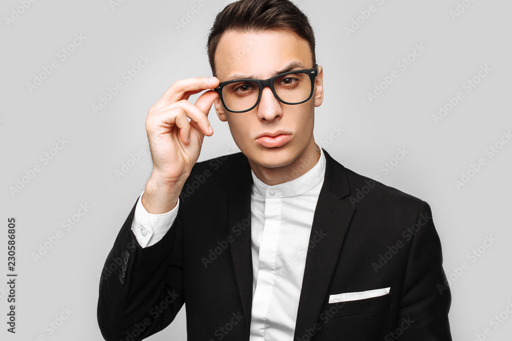Portrait of a handsome young business man, a man in a classic black suit and glasses, looking and wanting to see something, on a gray background. Portrait of a handsome young business man, a man in a classic black suit and glasses, looking and wanting to see something, on a gray background.