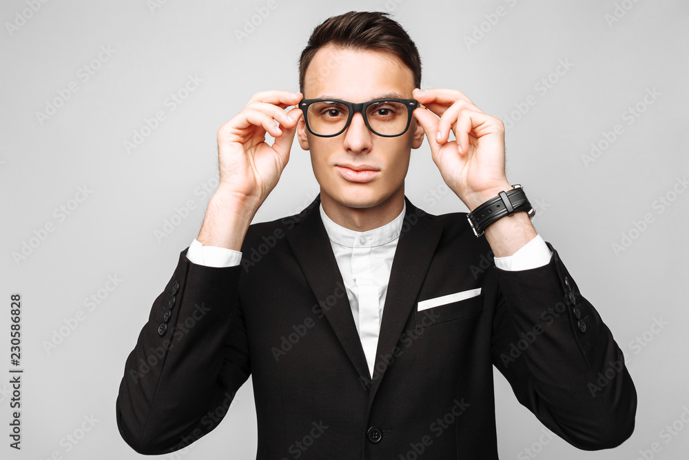 Portrait of a handsome young business man, a man in a classic black suit and glasses, looking and wanting to see something, on a gray background. Portrait of a handsome young business man, a man in a classic black suit and glasses, looking and wanting to see something, on a gray background.