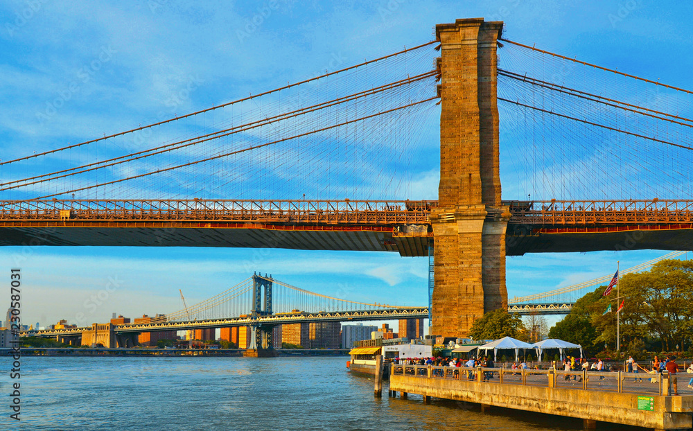 Naklejka premium Brooklyn promenade with famous Brooklyn bride and Manhattan bridge and river hudson in background against cloudy colorful blue sky in New York, USA
