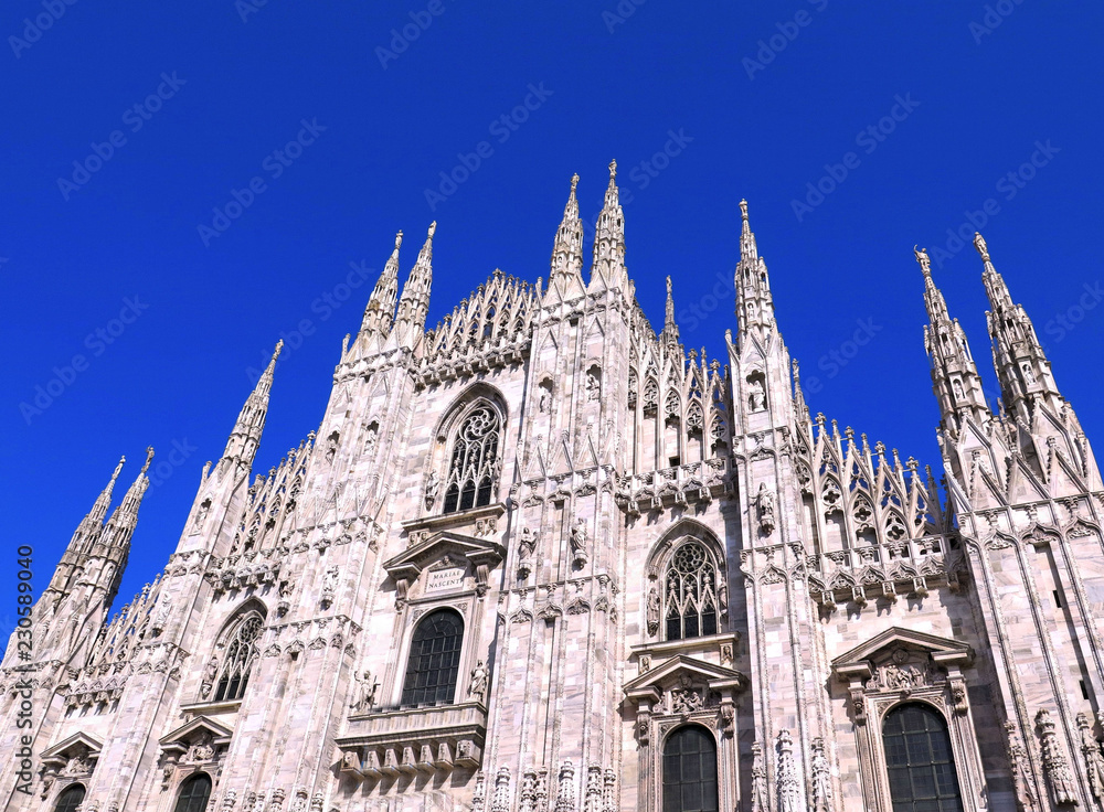 Detail of facade of famous Milan gothic Cathedral (Duomo di Milano) against blue sky on large square Piazza del Duomo, Italy          