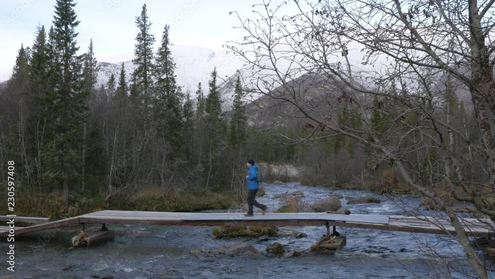 A man traveler crosses a mountain stream over a bridge. Beautiful view. A man traveler crosses a mountain stream over a bridge. Beautiful view.