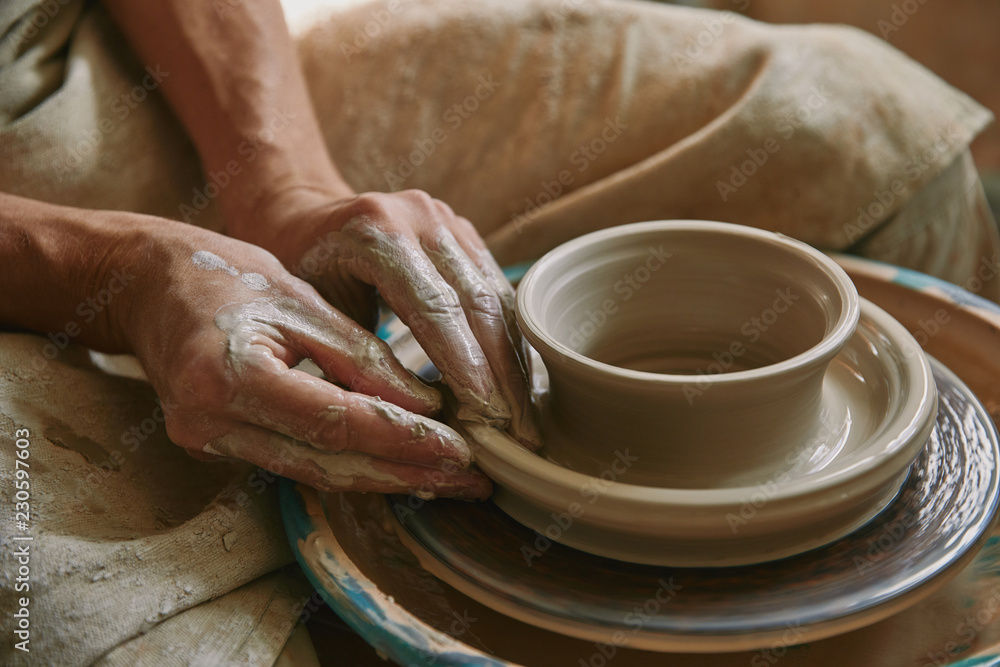 Close up view of professional potter working on pottery wheel at workshop