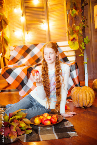 Red-haired teenager girl in a studio in the fall scenery with yellow leaves, apples and pumpkin