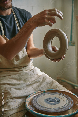 partial view of professional potter in apron holding clay at pottery studio