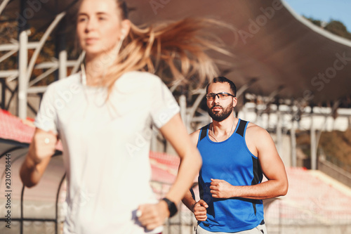 Sportish blonde long haired woman in white t-shirt and multicultural bearded man in blue shirt chasing each other at the football stadium outdoor, healthy lifestyle and people concept