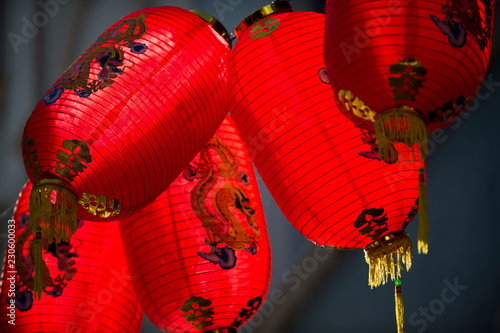 Traditional hanging red Chinese paper lanterns decorated with dragons blowing in the wind on a shadowed back alley