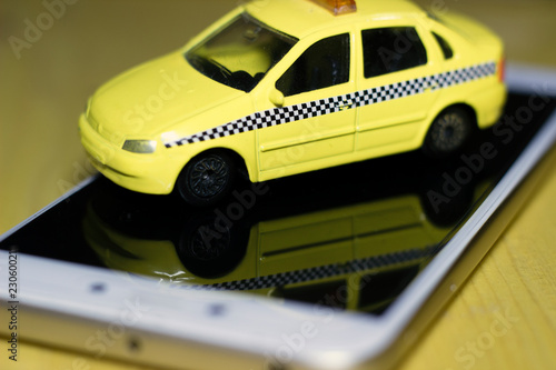 Yellow toy taxi car is standing on a white smartphone on a wooden surface, macro photography. texture background