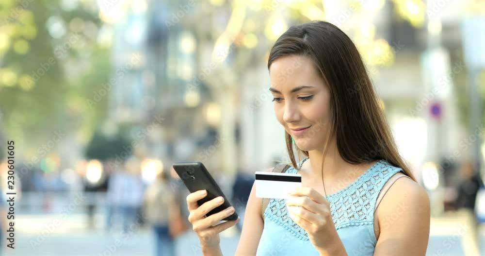 Happy woman paying online with credit card and a smart phone in the street. E-commerce concept Happy woman paying online with credit card and a smart phone in the street. E-commerce concept