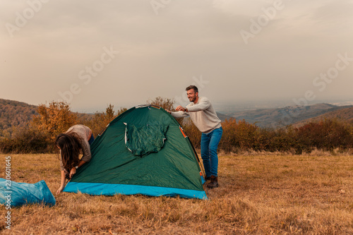 Young couple on a camping holiday raising tent together on a meadow.