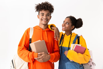 Photo of smiling african american students wearing backpacks holding exercise books, isolated over white background