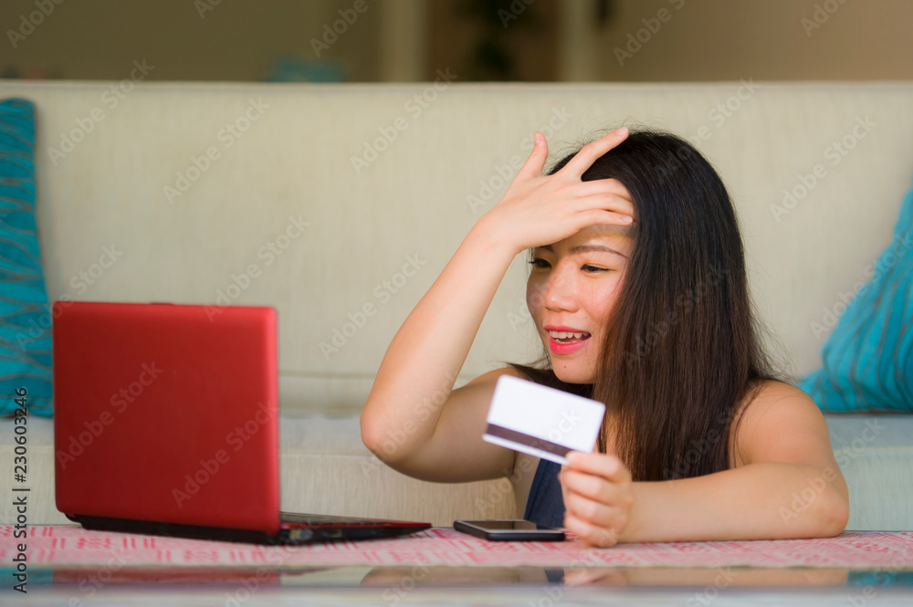 lifestyle portrait of young beautiful and happy Asian Korean woman holding credit card banking and online shopping with laptop computer at home couch in internet business lifestyle portrait of young beautiful and happy Asian Korean woman holding credit card banking and online shopping with laptop computer at home couch in internet business
