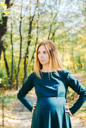 Beautiful portrait of pregnant woman belly in a warm dress in colorful autumn forest in September. The concept of pregnancy and the seasons