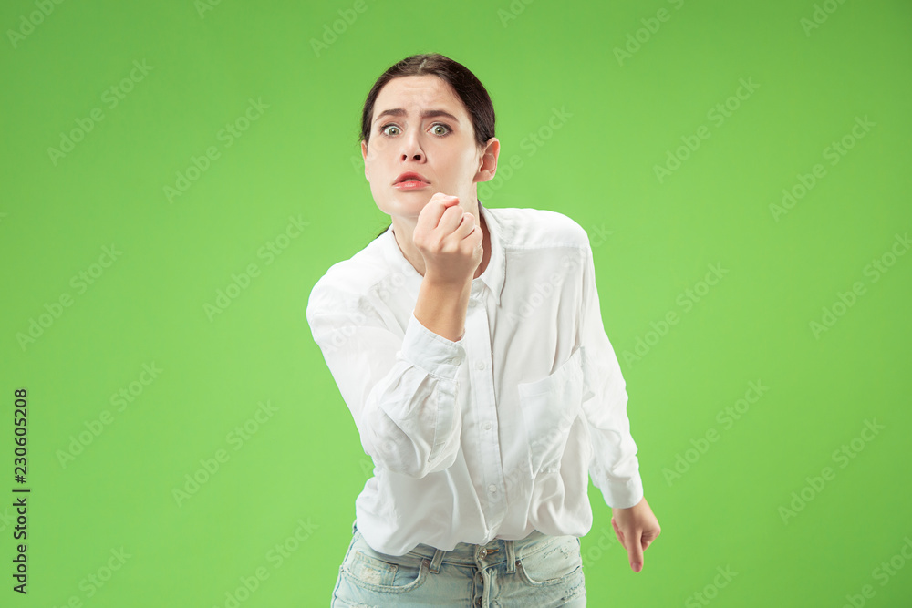 Angry woman looking at camera. Aggressive business woman standing isolated on trendy green studio background. Female half-length portrait. Human emotions, facial expression concept Angry woman looking at camera. Aggressive business woman standing isolated on trendy green studio background. Female half-length portrait. Human emotions, facial expression concept