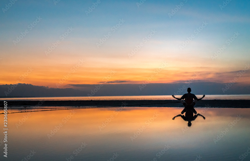 Young man meditating on the water with reflection during a beautiful sunset