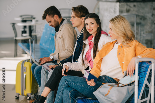 young people sitting together and waiting for flight in airport terminal