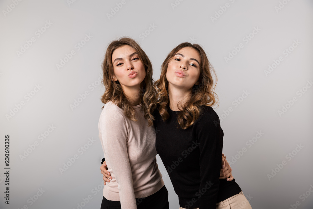 Image of two gorgeous girls smiling and posing together, isolated over gray background Image of two gorgeous girls smiling and posing together, isolated over gray background