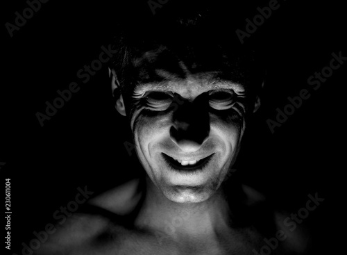 Stylish portrait of adult caucasian man. He smiles like maniac and seems like maniac or crazy. Black and white shot, low-key lighting. Angry man, fear concept.