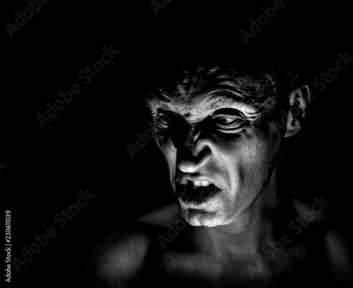 Stylish portrait of adult caucasian man with very angry face and who seems like maniac or devil. He screams at someone. Black and white shot, low-key lighting. Angry man, fear concept.