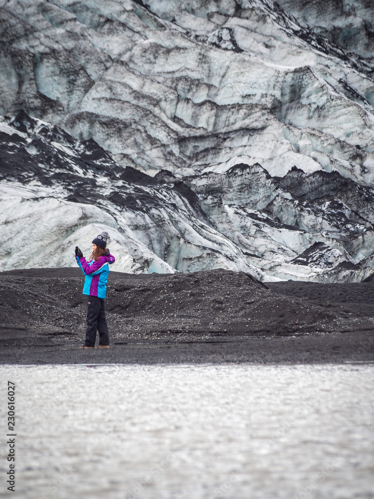 Lonely turist girl near a glacier taking pictures