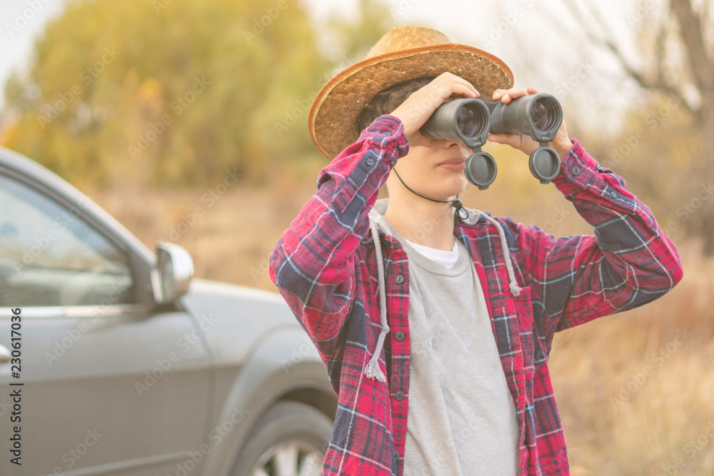 young man on a road trip with car using binocular and search the way f
