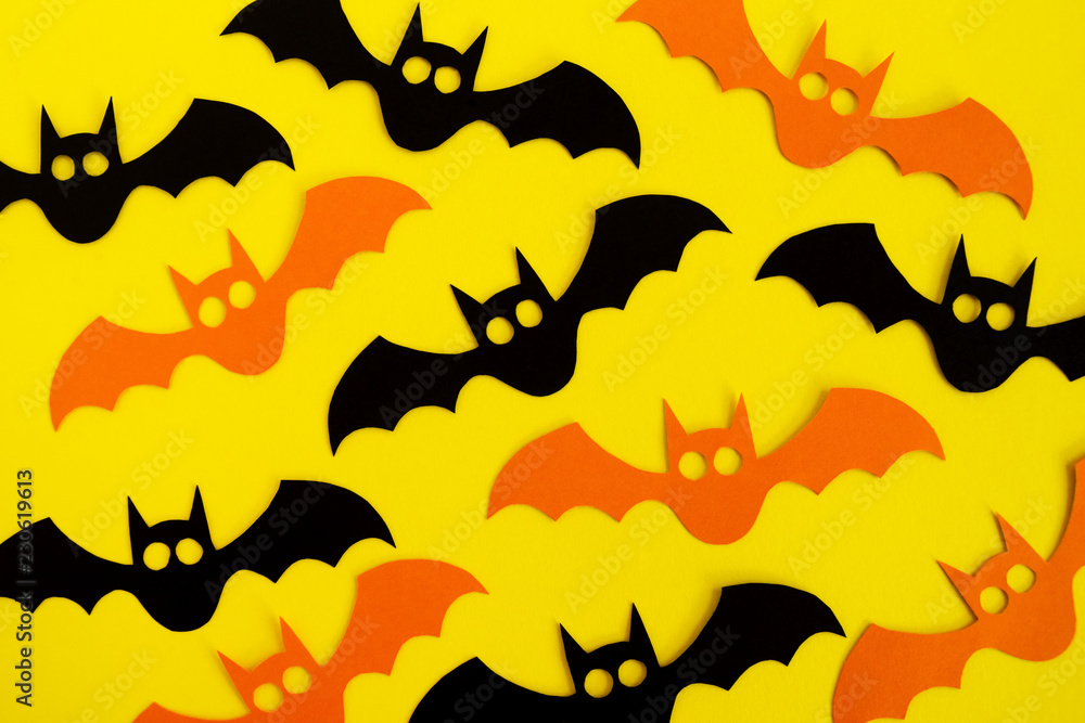 Holiday decorations for Halloween. Black and orange paper bats on a yellow background, top view.