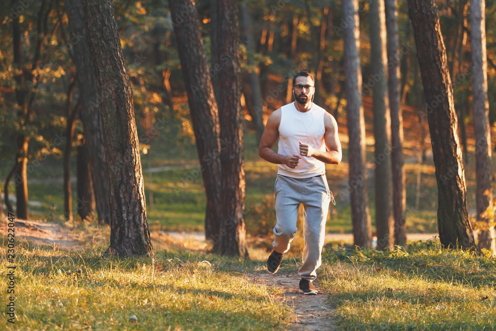 Fototapeta premium Multicultural handsome bearded man in sportswear jogging at the forest, healthy lifestyle and people concept