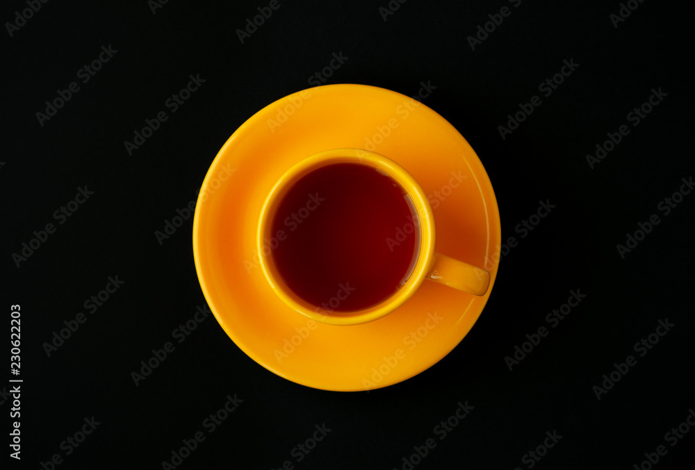 Yellow cup of tea on a black background. View from above. Contrast in the form of a yellow cup of tea in the middle of a black background. Classic tea in a contrasting setting.
