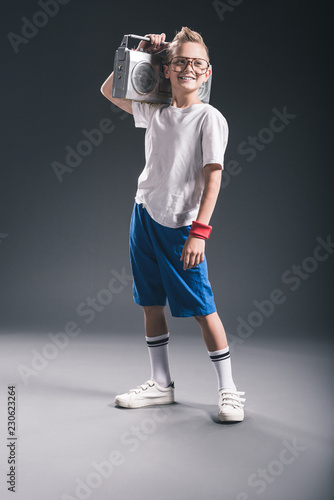 stylish preteen boy holding boombox on shoulder on grey backdrop