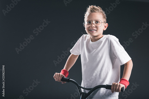 portrait of stylish boy in eyeglasses with scooter on black backdrop