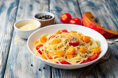 Spaghetti pasta with pumpkin, cherry tomatoes and parmesan cheese in white bowl on vintage wooden background. Selective focus.