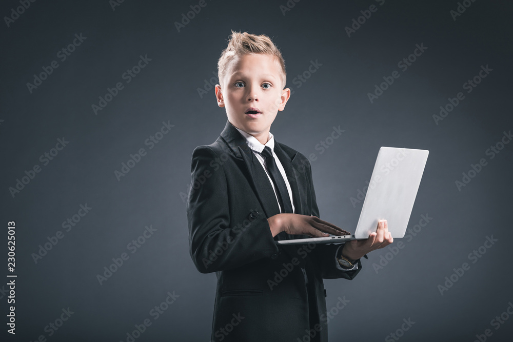 shocked little businessman with laptop looking at camera on grey backdrop shocked little businessman with laptop looking at camera on grey backdrop