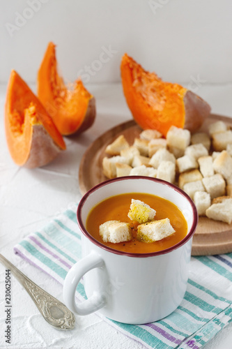 Delicate vegetable cream soup with pumpkin and croutons and slices of pumpkin on a light background.