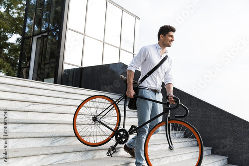Happy businessman dressed in shirt carrying a bicycle