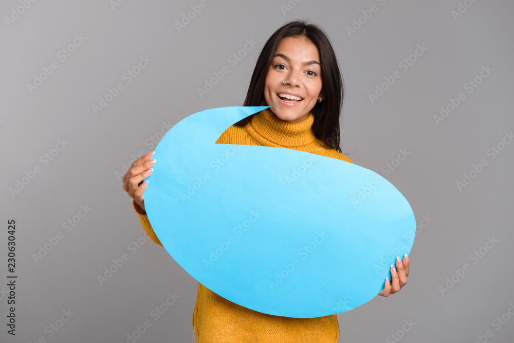 Fototapeta premium Happy woman posing isolated over grey wall background holding speech bubble.