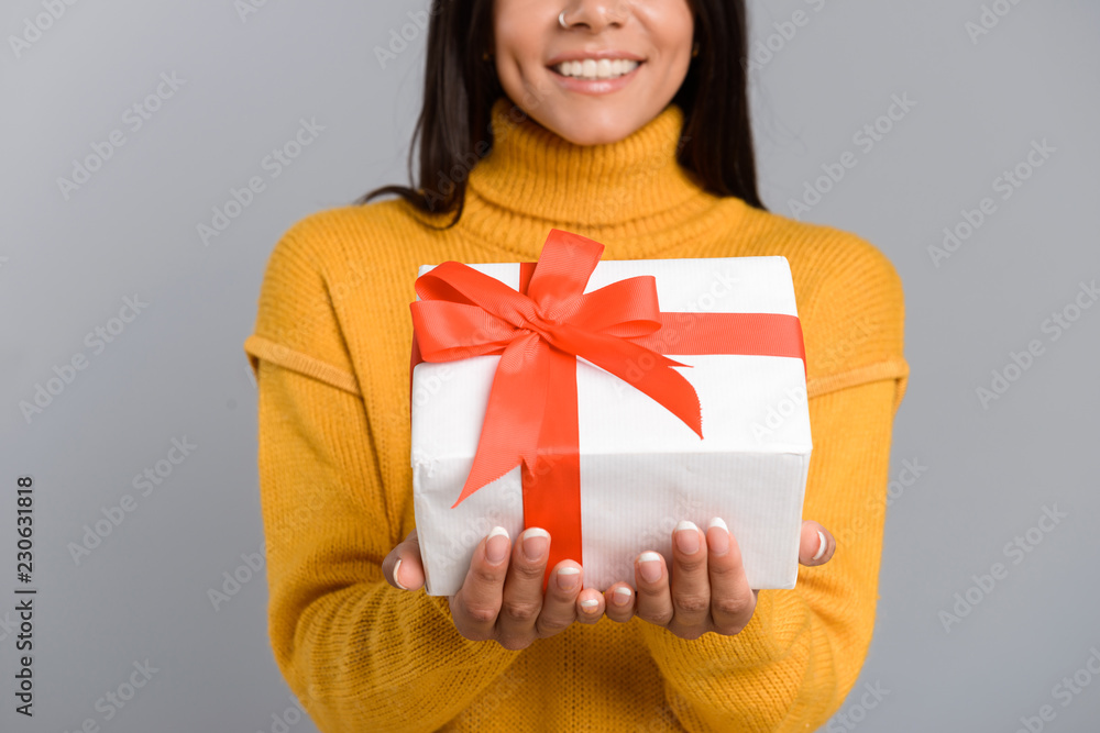 Cheerful woman posing isolated over grey wall background holding box surprise present. Cheerful woman posing isolated over grey wall background holding box surprise present.