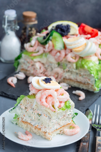 Piece of traditional savory swedish sandwich cake Smorgastorta with bread, shrimps, eggs, caviar, dill, mayonnaise, cucumber and lettuce, vertical