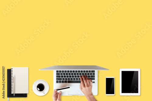 technology working table with woman hands on laptop computer, credit card, coffee cup and cell phone on yellow background (or shopping and payment online concept)