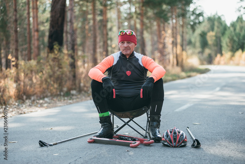 Training an athlete on the roller skaters. Biathlon ride on the roller skis with ski poles, in the helmet. Autumn workout. Roller sport. Adult man riding on skates. Athlete is getting ready to start. photo