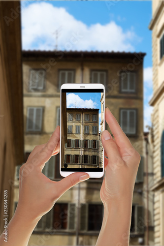 A tourist is taking a photo of part of the facade of an old residential building in the historic part of Florence, Italy on a mobile phone