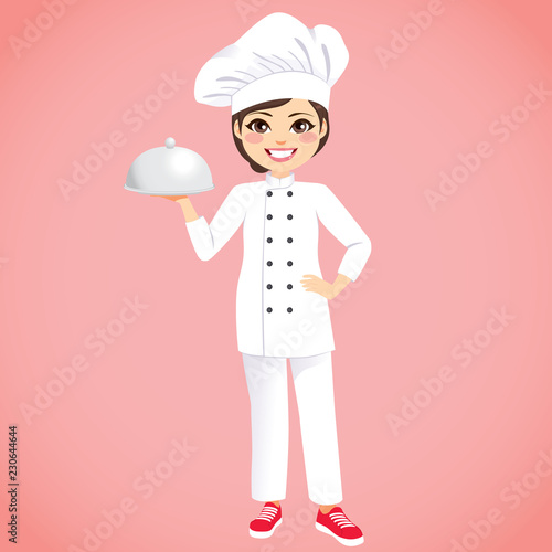 Young beautiful happy female chef wearing white uniform holding silver tray on pink background