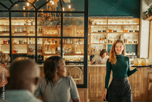 Smiling waitress bringing drinks to people sitting in a bar photo