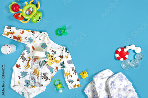 Babies goods: cloth diaper, baby powder, nibbler, cream, teether, soother, baby toy on blue background. Copy space. Top view. photo