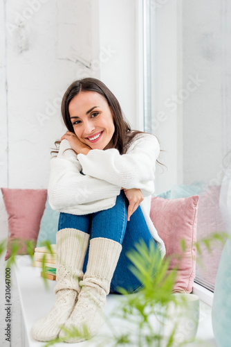 attractive young woman relaxing on windowsill with cushions at home