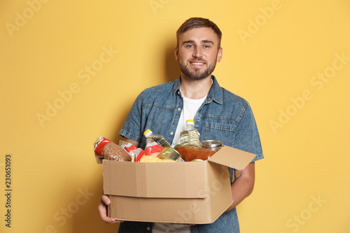 Young man holding box with donations on color background photo