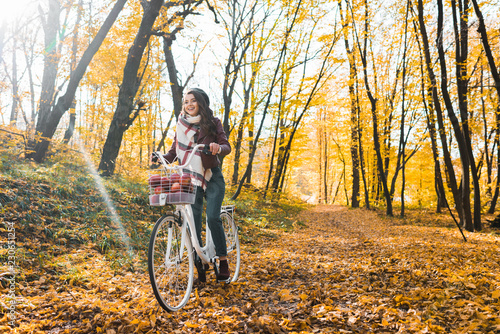 selective focus of happy girl in leather jacket and beret riding on bicycle in yellow autumnal forest