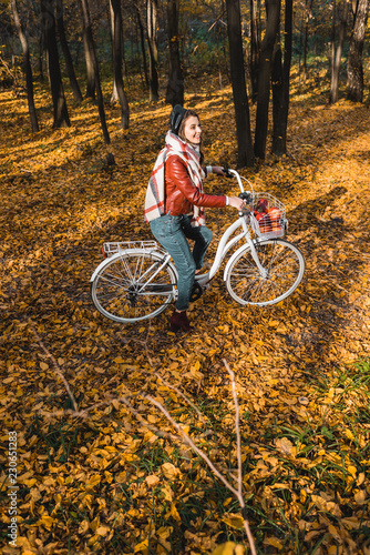 high angle view of girl in leather jacket and beret riding on bicycle in yellow autumnal forest