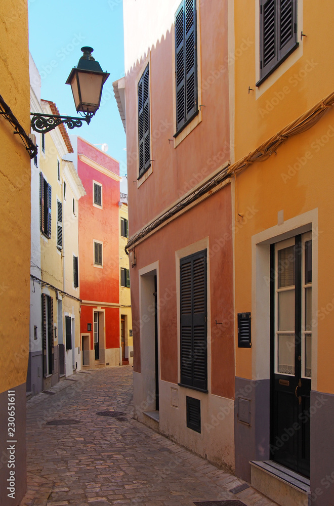 A beautiful narrow quiet street of brightly painted old houses in summer sunlight in ciutedella menorca