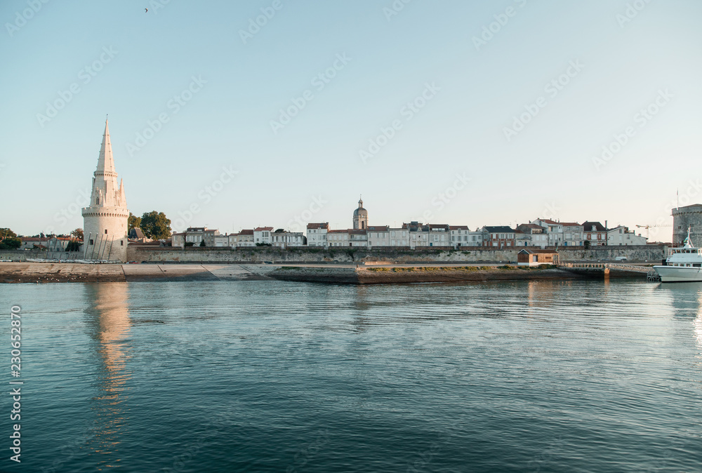 Naklejka premium La Rochelle, France: 26 August 2018: Embankment at the La Rochelle city on the coast of Atlantic ocean with medieval fortification towers. Early morning, sunrise