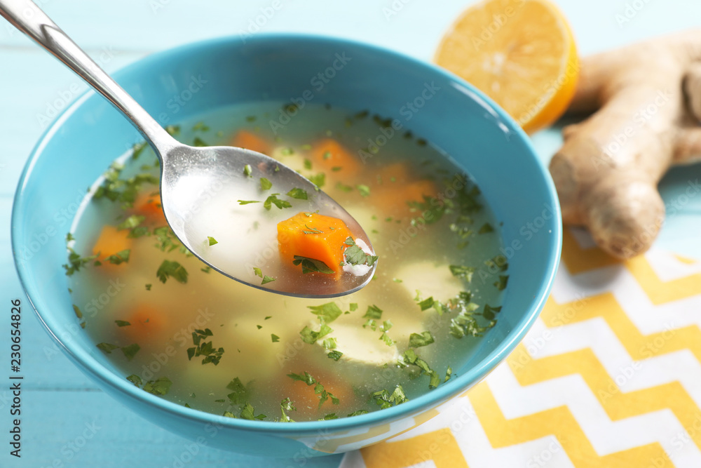 Spoon with fresh homemade soup to cure flu over bowl on wooden table Spoon with fresh homemade soup to cure flu over bowl on wooden table