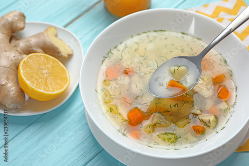 Spoon with fresh homemade soup to cure flu over bowl on wooden table